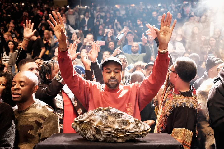 A crowd raises their hands around a large oyster on a table.